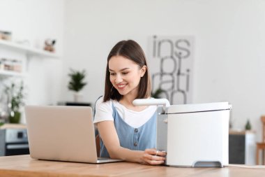 Young woman with deep fryer using laptop in kitchen