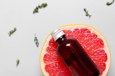Gri arka planda bir şişe gerekli yağ ve greyfurt.