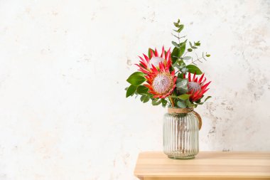 Odada ışık duvarının yanında protea çiçekleri olan masa.