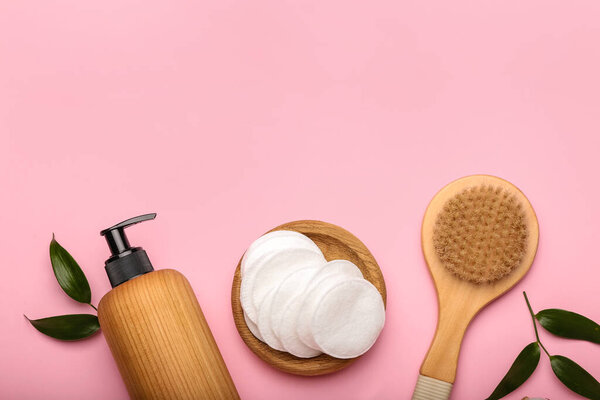 Держатель с хлопчатобумажными прокладками, щеткой и бутылкой косметического средства на цветном фоне