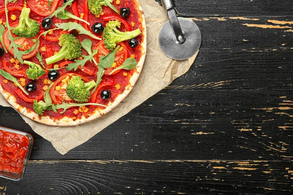 Parchment with tasty vegetarian pizza and sauce on dark wooden background