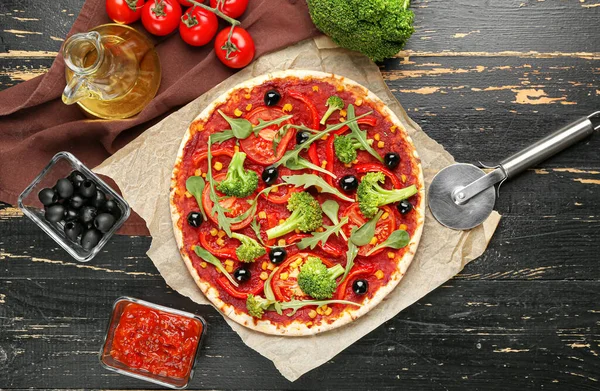 Parchment with tasty vegetarian pizza and sauce on dark wooden background