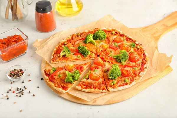 Board with tasty vegetarian pizza, sauce and peppercorn on light background