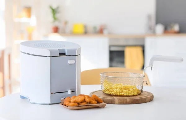 Modern deep fryer with french fries and nuggets on table in kitchen