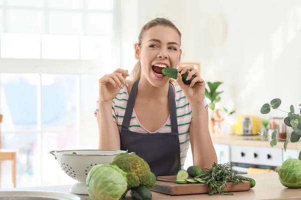 年轻女人在厨房里吃黄瓜 — 图库照片
