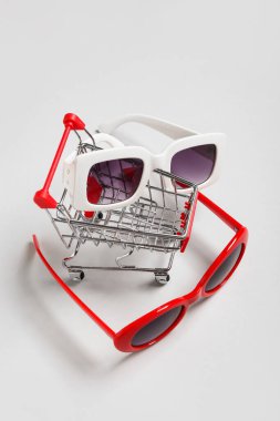 Gri arka planda şık güneş gözlüklü alışveriş arabası.