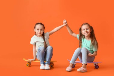 Cute little sisters with skateboards on color background