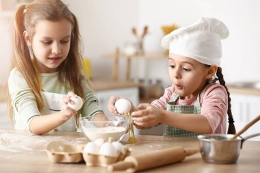 Cute little sisters breaking eggs into bowl in kitchen