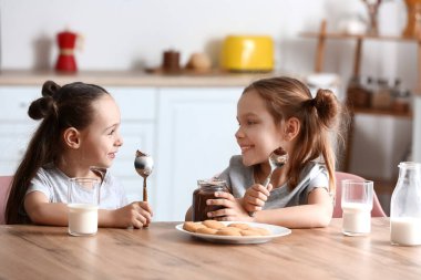 Cute little sisters eating chocolate paste in kitchen