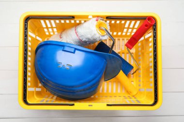 Beyaz ahşap arka planda boyacı malzemeleri olan alışveriş sepeti.