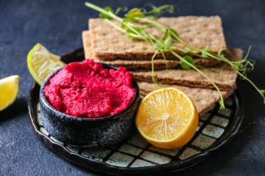 Koyu arkaplanda pancar humus, limon ve kraker olan bir kase, yakın plan.