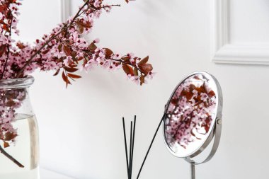 Vase with blossoming branches and mirror near light wall