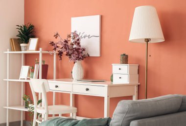 Renk duvarının yanında vazosu ve çiçek açan dalları olan modern bir işyeri.