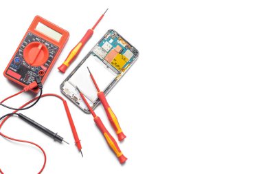 Disassembled mobile phone with multimeter on white background
