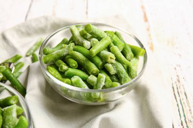 Bowl with frozen green beans on light wooden background