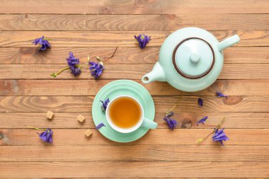 Cup with tasty floral tea and teapot on wooden background