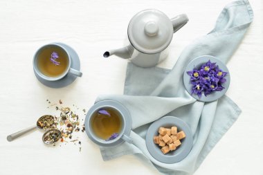 Cups with tasty floral tea and teapot on light wooden background