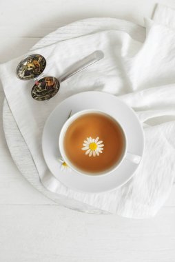 Cup of floral tea and infuser on light wooden background