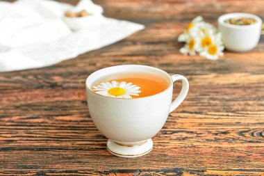 Cup of floral tea and chamomile flowers on wooden background