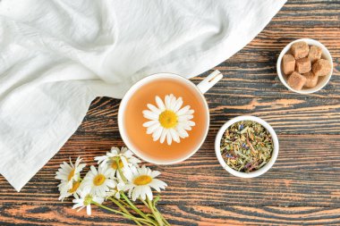 Composition with cup of tea, dry herbs, sugar and flowers on wooden background
