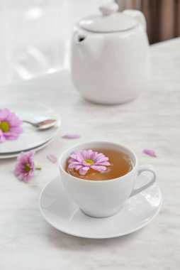 Cup of floral tea, teapot and flowers on table in room