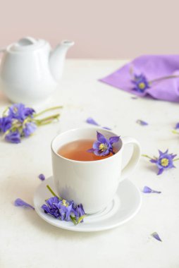 Cup of floral tea and flowers on light background