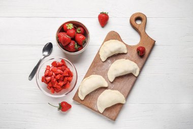 Composition with raw dumplings and strawberry on light wooden background