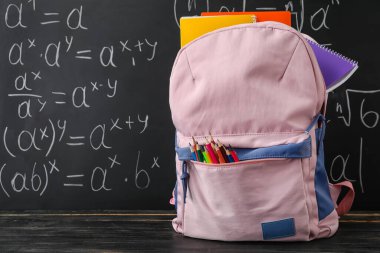School backpack with stationery on table near blackboard
