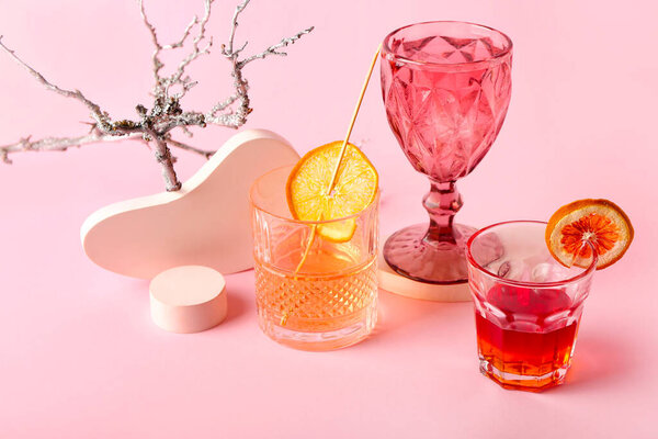 Glasses of tasty cocktails and tree branch on color background