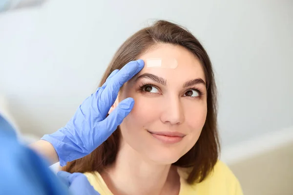 Nurse applying medical patch on young woman\'s forehead in clinic