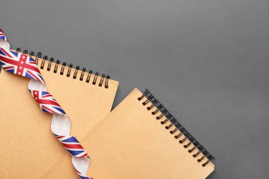 Gri arkaplanda İngiliz bayrağı renginde not defterleri ve kurdeleler. İngilizce öğrenme kavramı