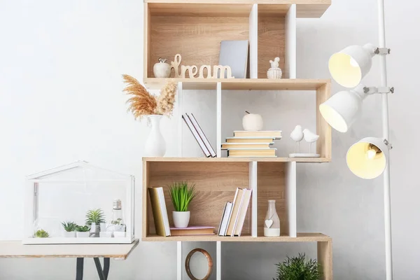 Stylish shelf unit with books and decor near light wall