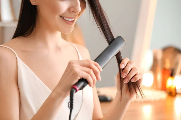 Beautiful young woman straightening hair at home