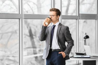 Genç adam ofiste kahve içiyor.