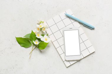 Cep telefonu, defter, kalem ve yasemin çiçekleri açık arkaplanda