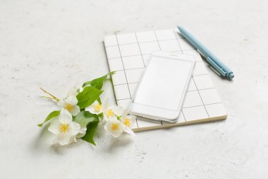 Cep telefonu, defter, kalem ve yasemin çiçekleri açık arkaplanda