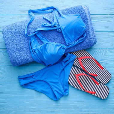 Şık bir mayo, havlu ve tahta arka planda parmak arası terlikler.