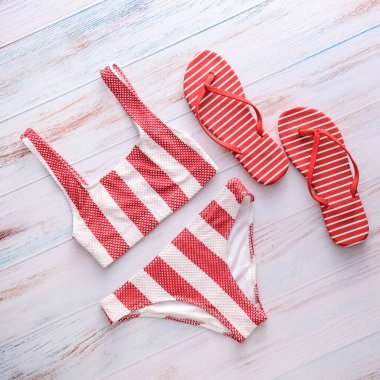 Şık bir mayo ve hafif ahşap arka planda parmak arası terlikler.