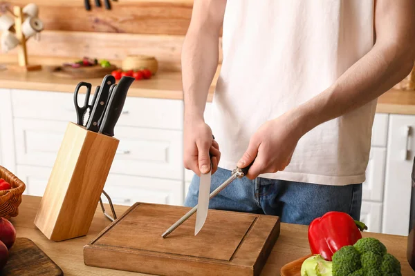 Man sharpening knife in kitchen, closeup