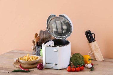 Modern fritöz, lezzetli patates kızartması ve sebzeler renkli duvarın yanındaki masada.