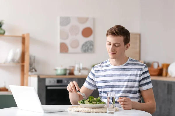 Young man eating fresh salad in kitchen