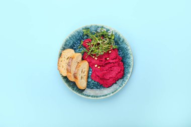 Lezzetli pancar humusu tabağı, taze lahanalar ve renkli arka planda ekmek.