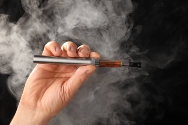 Esmer arka planda elektronik sigaralı erkek eli dumanlı.