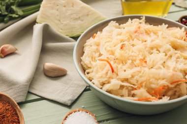 Lezzetli lahana turşusu ve ahşap arka planda malzemelerle dolu bir kase.