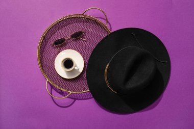 Tepsisi olan şık bir şapka, bir fincan kahve ve arka planda güneş gözlüğü.