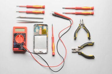 Gri arkaplanda teknisyen araçları olan parçalanmış cep telefonu