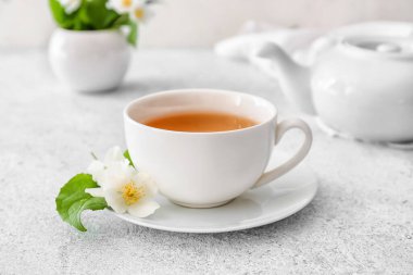 Bir fincan yasemin çayı, çaydanlık ve hafif arka planda çiçekler.