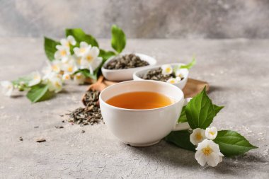 Bir fincan yasemin çayı, kuru yapraklar ve arkaplanda çiçekler ile kompozisyon