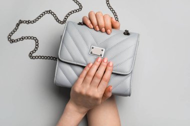 Güzel manikürlü eller ve gri arka planda çanta.