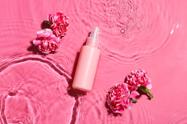 Bottle of cosmetic product and flowers in water on color background